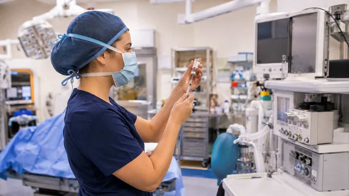 Nurse anesthesia student in navy scrubs drawing up medication beside an anesthesia machine in the operating room