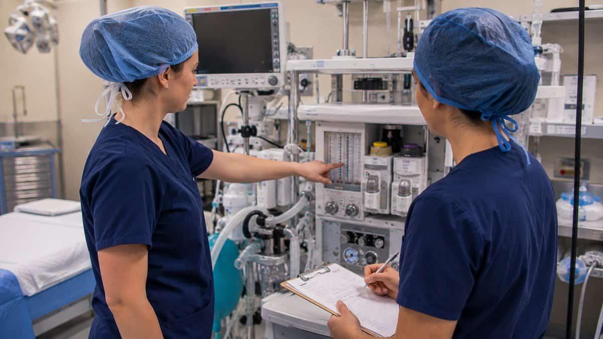 Two nurse anesthesia students reviewing the anesthesia machine together in an operating room