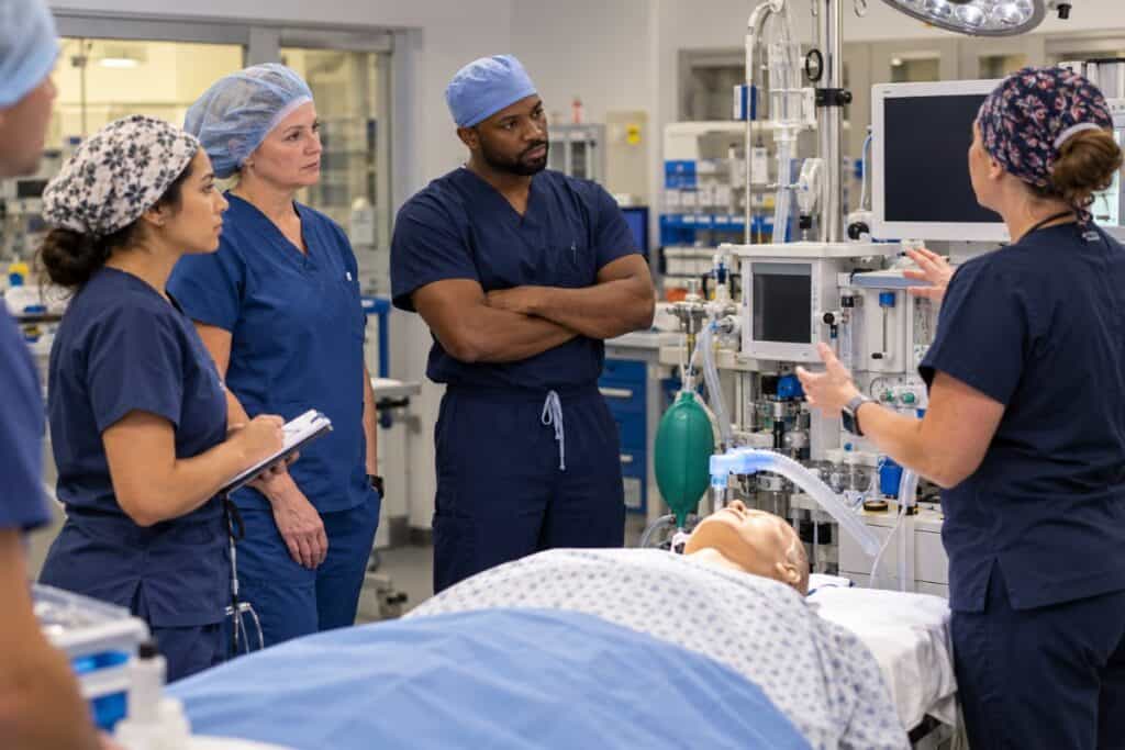 Nurse anesthesia students listening to an instructor beside a patient simulator in a simulation lab